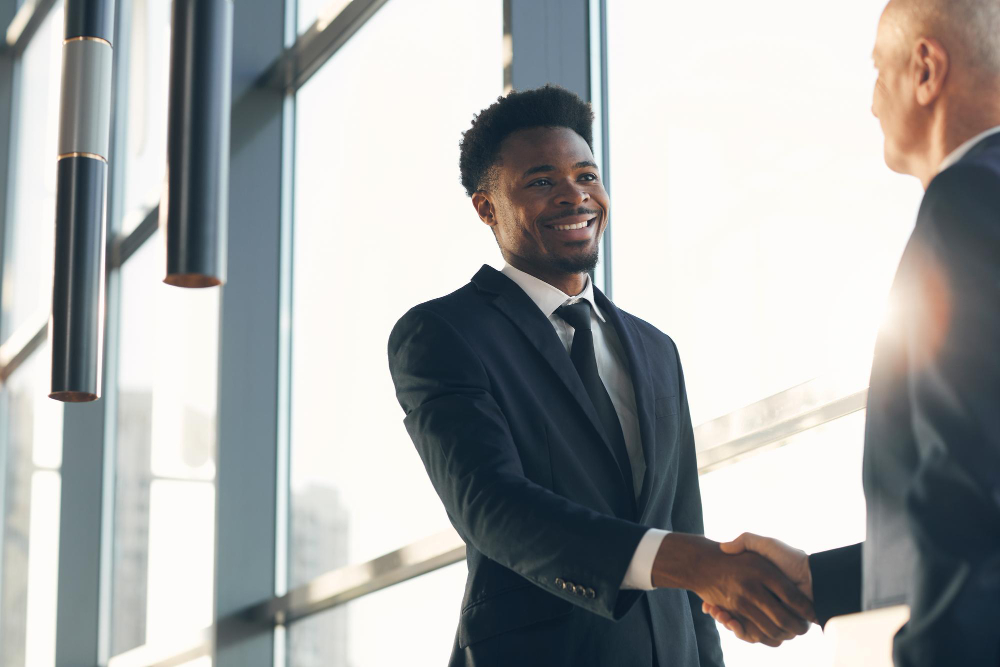 Homme noir souriant validant un contrat client avec homme blanc souriant.